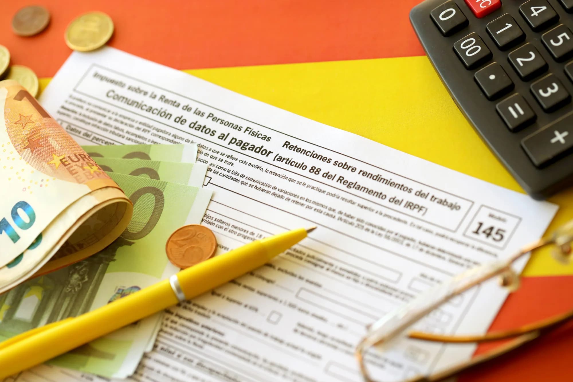 Un documento financiero con un bolígrafo, una calculadora, monedas y billetes de euro sobre una superficie de colores vivos. Los billetes y monedas rodean el formulario, transmitiendo atención al detalle y organización.