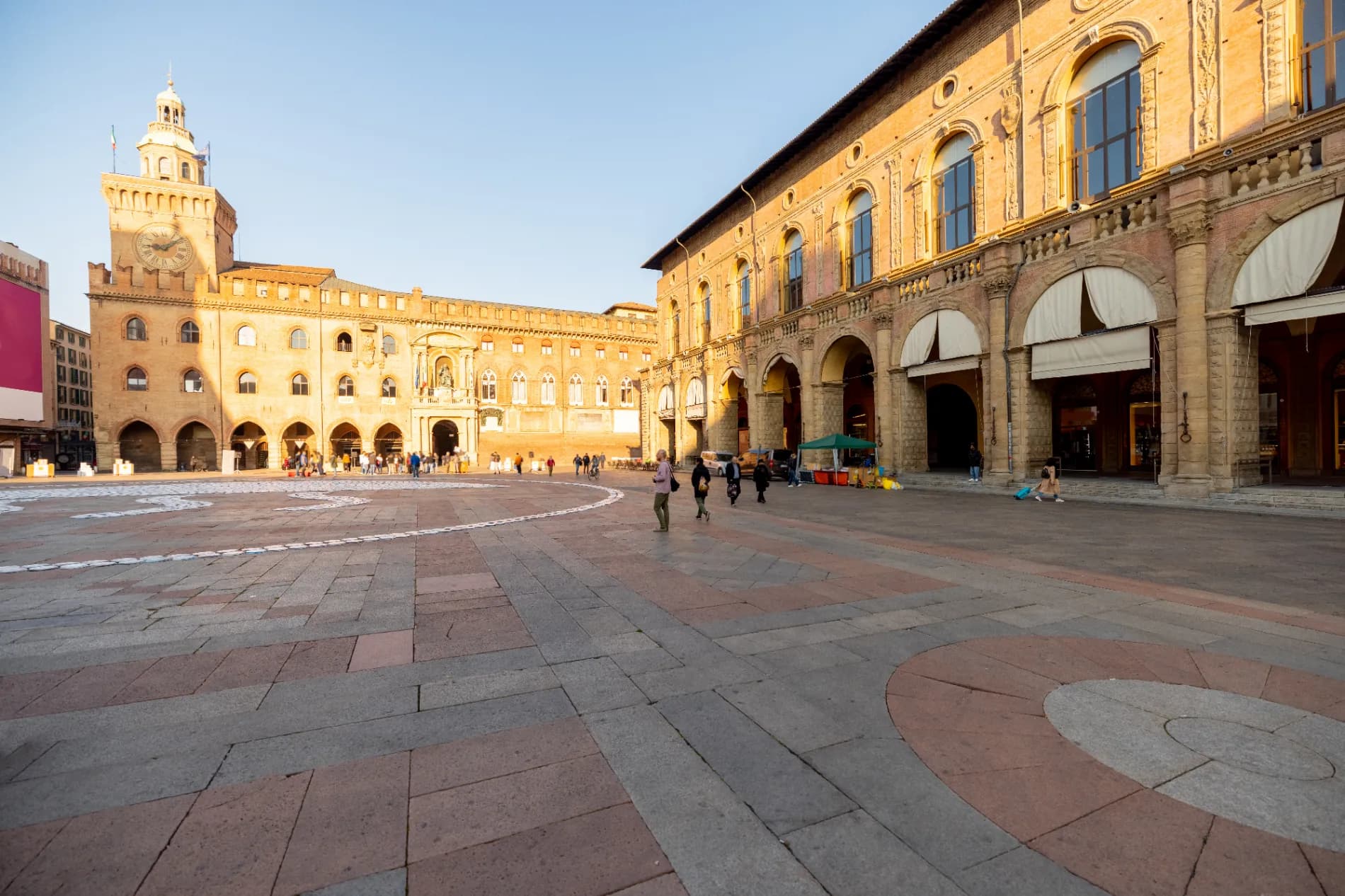 Sunlit Italian piazza at dawn with a few early walkers and cafe tables set up for morning service