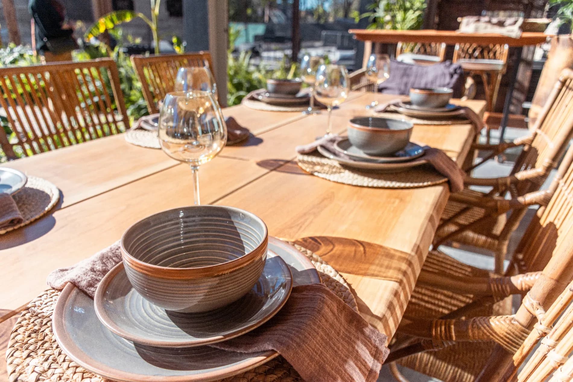 A long wooden table outdoors set for a leisurely Italian lunch with pasta, wine, and family