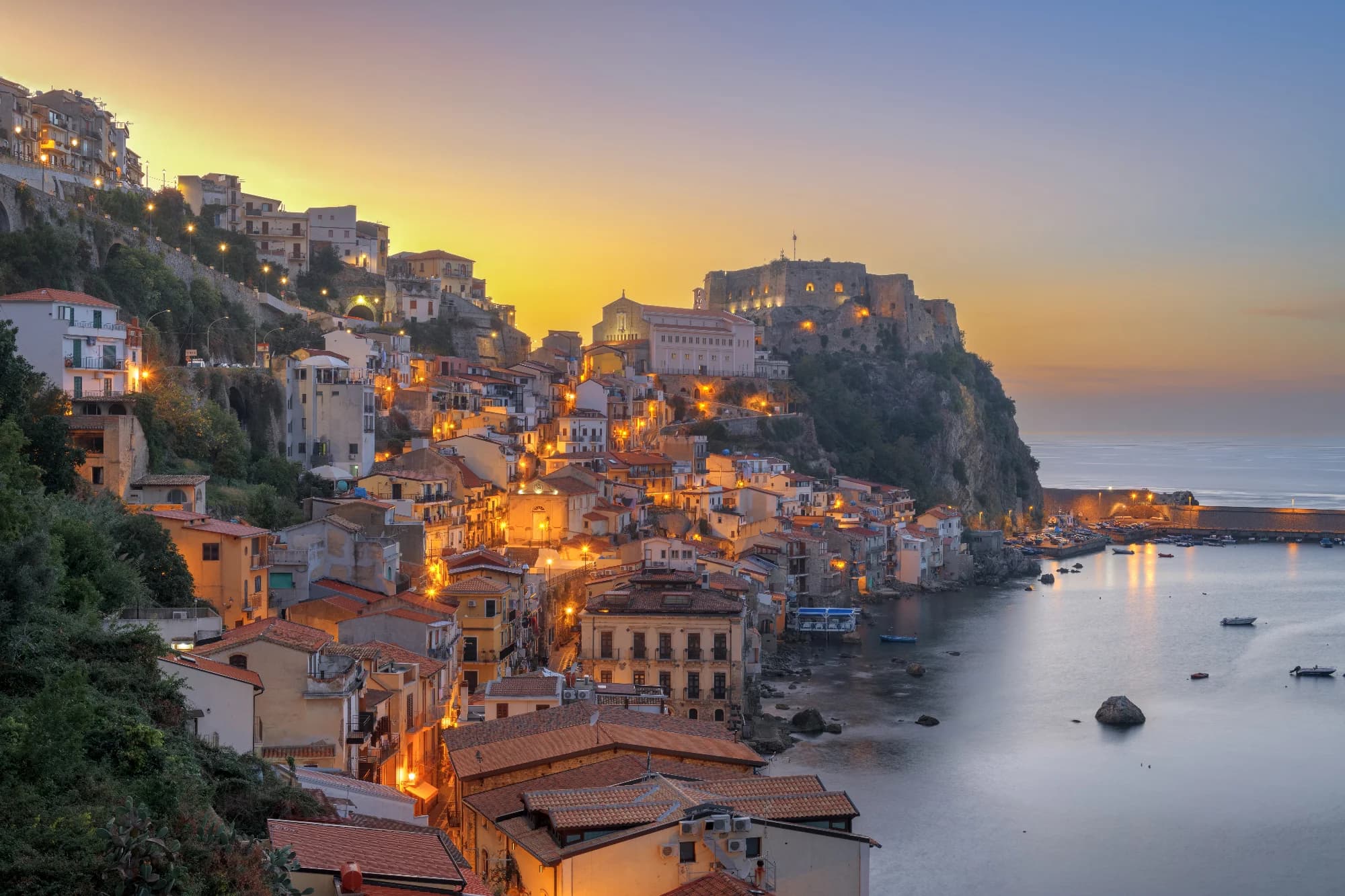 A quiet Italian coastal village at sunset with warm light washing over pastel houses