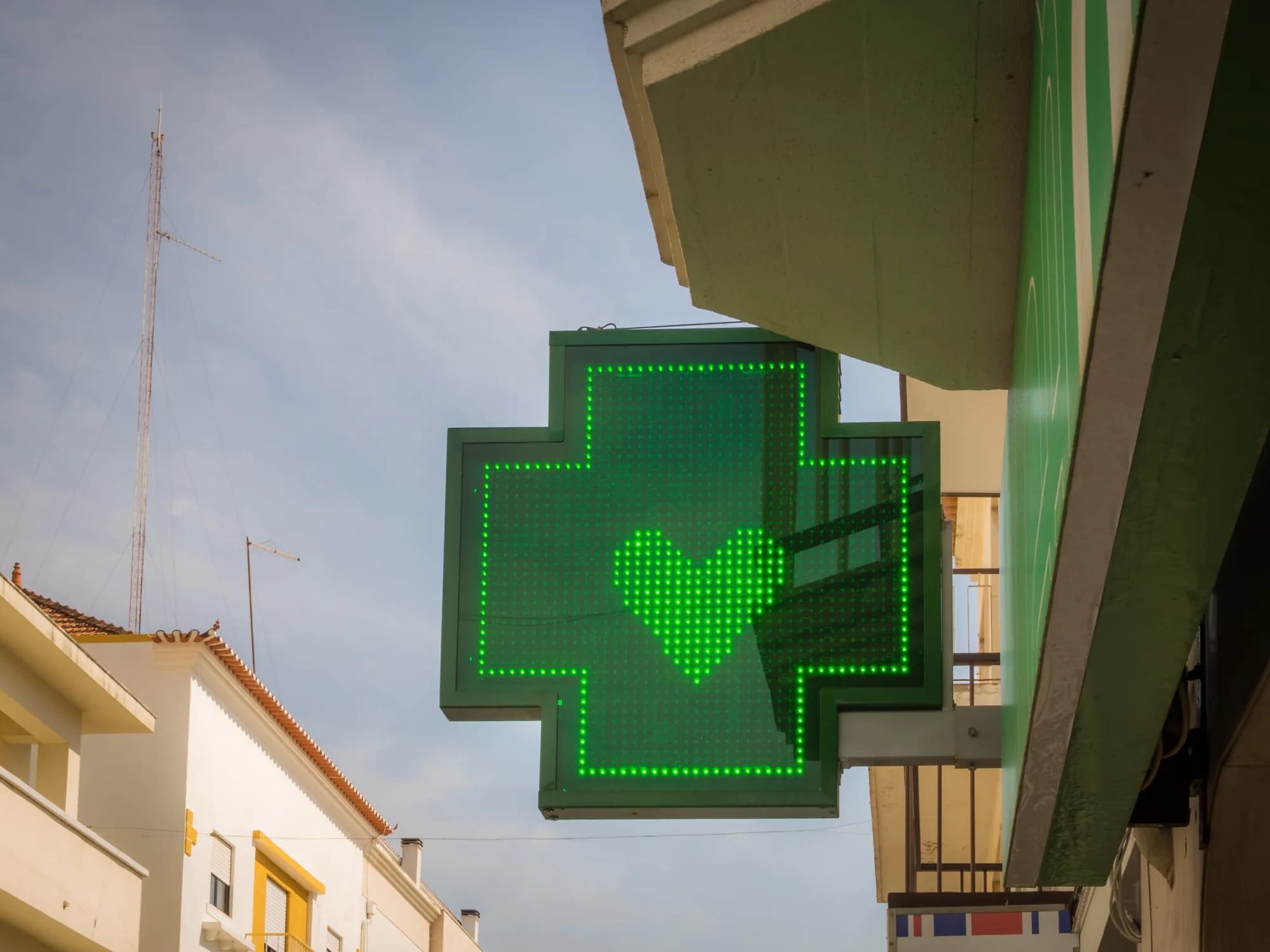 Calm morning light over a Mediterranean coastal town with a pharmacy green cross visible on a whitewashed facade