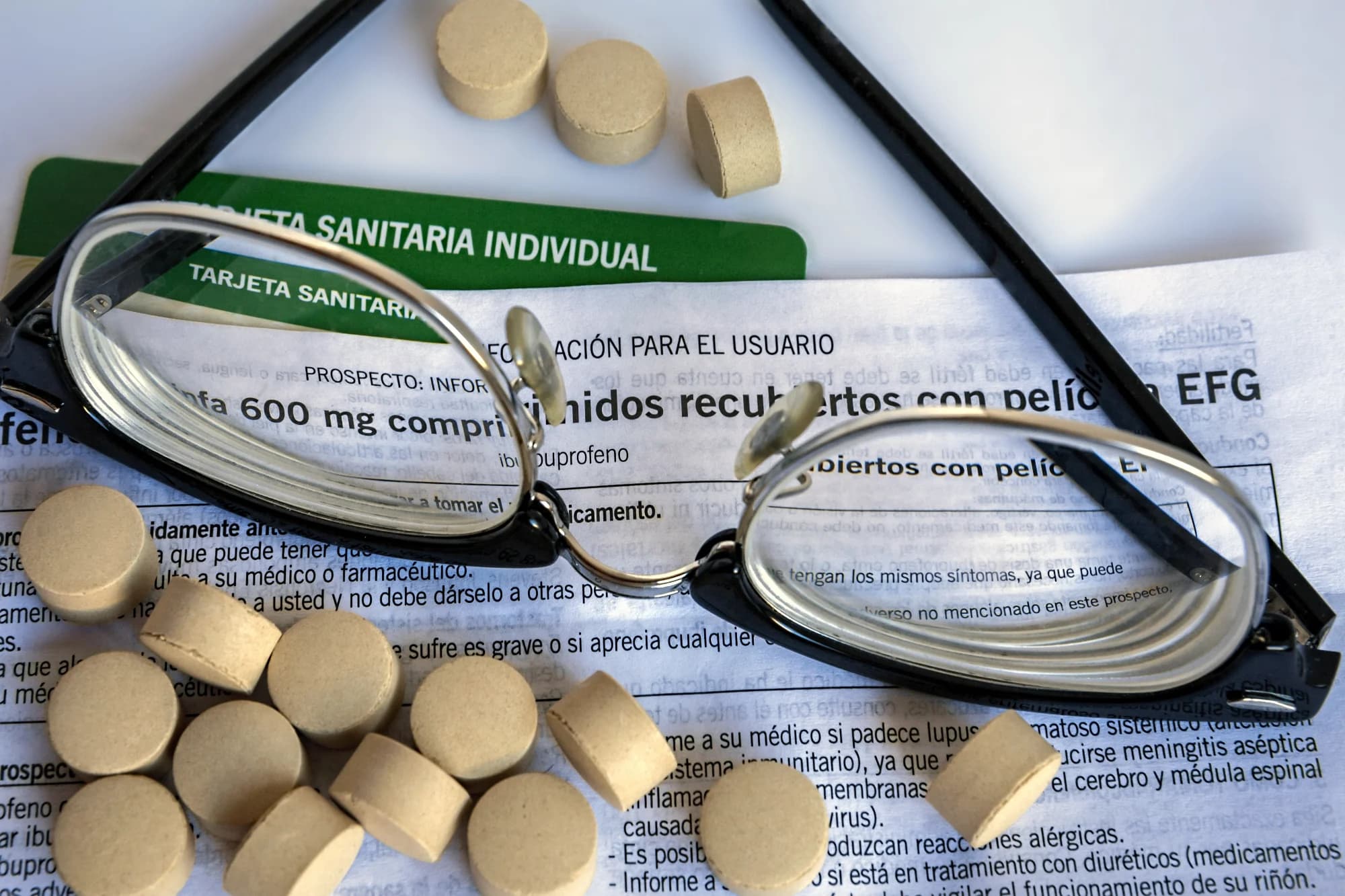 Close-up of a Spanish public health card (tarjeta sanitaria) resting on a wooden desk next to reading glasses